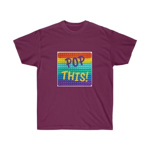 May include: A maroon t-shirt with a rainbow pop-it toy graphic and the text "POP THIS!" printed on the front.