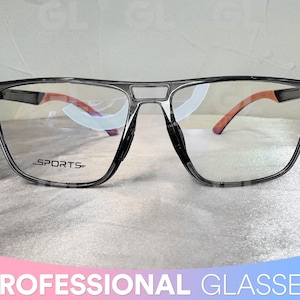 May include: Grey sports glasses with a black frame and clear lenses. The frame has the word "SPORTS" printed on the side.