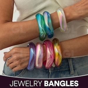 May include: A collection of iridescent jewelry bangles in various colors, including green, blue, purple, pink, and gold. The bangles are worn on the wrists, showcasing their glossy, translucent appearance. The text "JEWELRY BANGLES" is displayed at the bottom.