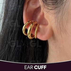 May include: A gold ear cuff with a three-loop design. The ear cuff is shown on an ear. The text "EAR CUFF" is at the bottom of the image.