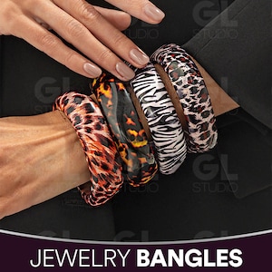 May include: A collection of four bangles with animal print designs. The bangles feature patterns such as leopard print, tortoise shell, and zebra stripes. The jewelry is displayed on a person's arm. The text "JEWELRY BANGLES" is at the bottom of the image.