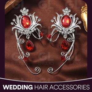 May include: Two silver-toned wedding hair accessories with red gemstones. Each piece features a large oval red gem at the center, surrounded by smaller clear crystals and teardrop-shaped red gems. The text "WEDDING HAIR ACCESSORIES" is at the bottom.