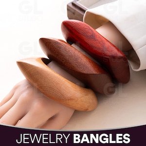 Puede incluir: Se muestran tres brazaletes de madera en tonos marrones y rojos. Los brazaletes tienen un diseño liso y curvado, con vetas de madera visibles. El texto "JEWELRY BANGLES" está en la parte inferior de la imagen.