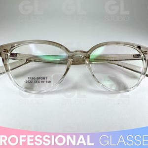 May include: Transparent-framed spectacles with a rounded shape and a subtle cat-eye design. The glasses have a clear frame and lenses, with the text "TR90-SPORT 12922 55 019-149" visible on the lens. The image also includes the text "PROFESSIONAL GLASSES".