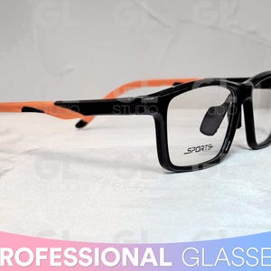 May include: Black and orange sports glasses with a black frame and clear lenses. The frame has the word "SPORTS" printed on the side.