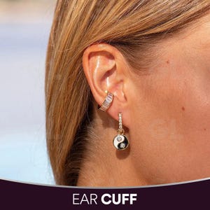 May include: A gold-toned ear cuff with rectangular clear stones and a dangling earring. The earring features a black and white yin-yang design with clear stones and a gold-toned setting. The text "EAR CUFF" is at the bottom.