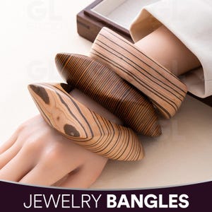 May include: Three wooden bangles with a natural wood grain pattern. The bangles are various shades of brown and tan. The text "JEWELRY BANGLES" is at the bottom of the image.