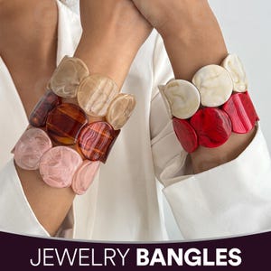 Op de afbeelding: Twee dikke sieradenarmbanden met grote, afgeronde, kleurrijke kralen. Eén armband heeft roze, bruine en bruinachtige kralen. De andere armband heeft rode en crèmekleurige kralen. De tekst "JEWELRY BANGLES" staat onderaan de afbeelding.