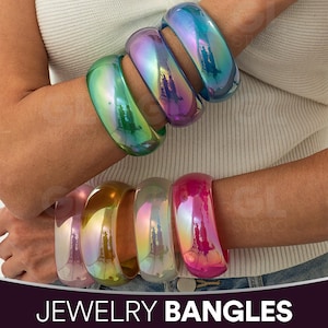 Peut inclure: Plusieurs bracelets irisés aux couleurs vives, dont le vert, le violet et le rose, sont présentés sur des poignets. Les bracelets brillants reflètent la lumière. Le texte "JEWELRY BANGLES" est visible en bas de l'image.