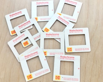 Può includere: Una collezione di dieci supporti per diapositive Kodachrome vintage. I supporti sono bianchi con un bordo rosso e il testo "Kodachrome Slide Diapositive" stampato in rosso. I supporti sono tutti in buone condizioni e hanno un leggero ingiallimento dovuto all'età.