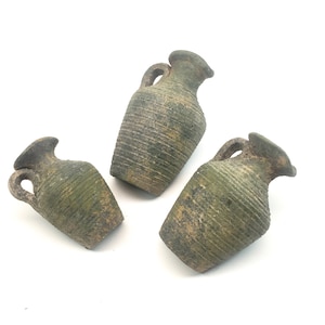 Peut inclure: Trois petites amphores de style antique à l'aspect vieilli et texturé. Les vases sont d'un vert sourd avec des accents bruns, avec des détails côtelés et de petites anses. Elles sont disposées sur un fond blanc.