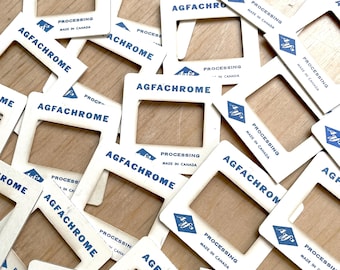 Può includere: Primo piano di una pila di supporti per diapositive Agfachrome vintage. I supporti sono bianchi con testo blu che recita "Agfachrome" e "Elaborazione Effettuata in Canada".