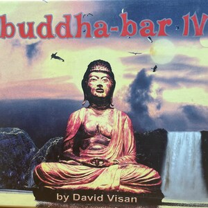 May include: The album cover for "buddha-bar IV" displays a seated Buddha statue in a tranquil pose. The statue is reddish-brown, set against a backdrop of a waterfall, mountains, and a sunset sky. The artist's name, David Visan, is at the bottom.