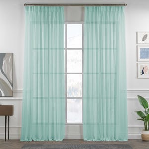 Puede incluir: Dos cortinas transparentes de color azul claro cuelgan delante de una ventana. Las cortinas están hechas de una tela ligera que permite que la luz pase a través de ellas.