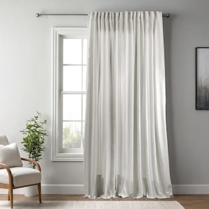 May include: A pair of white, floor-length curtains hang from a silver rod in front of a window. The curtains are made of a soft, flowing fabric. A white window frame is visible behind the curtains. A chair and plant are in the foreground.
