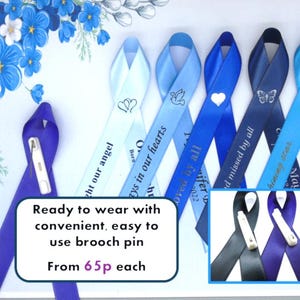 May include: A collection of satin awareness ribbons in various shades of blue, featuring printed symbols like hearts, doves, butterflies, and stars. Each ribbon includes a white brooch pin on the back for attachment, with text reading Ready to wear with convenient, easy to use brooch pin.