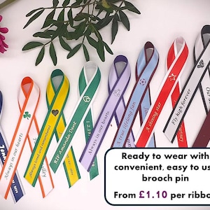 May include: A collection of colourful awareness ribbons featuring various printed text and symbols, including hearts, stars, and doves. Each ribbon is designed with a loop at the top and a metal brooch pin on the back for attachment, displaying phrases like Fly high forever and Always in our hearts.