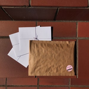 May include: A brown paper bag with a pink circle sticker that says "Handmade with love" in black text. The bag is tied with a string and has three white envelopes inside.