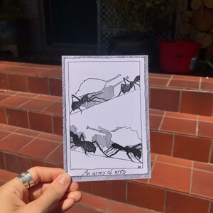 May include: A black and white illustration of ants carrying leaves. The illustration is on a white card with a black border. The text "An army of ants" is written at the bottom of the card.