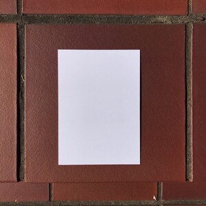 May include: A blank white card on a red brick background.
