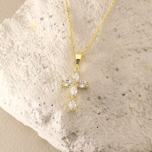 May include: A gold chain necklace with a small, clear crystal cross pendant.