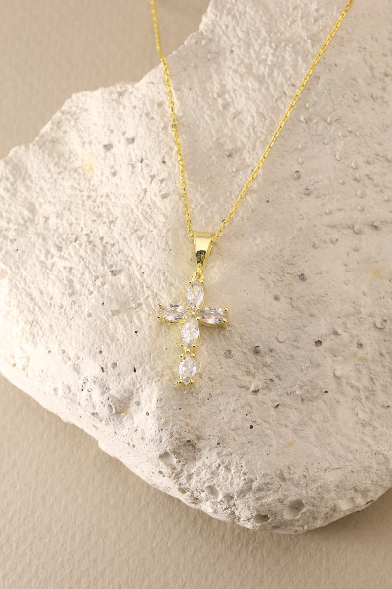 May include: A gold chain necklace with a small, clear crystal cross pendant.