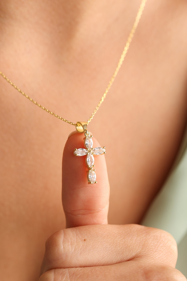 May include: A gold chain necklace with a small, clear crystal cross pendant.
