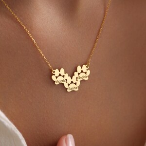 May include: Gold necklace with three paw print charms, each with a name engraved on it: Victoria, Sasha, and Sophie.