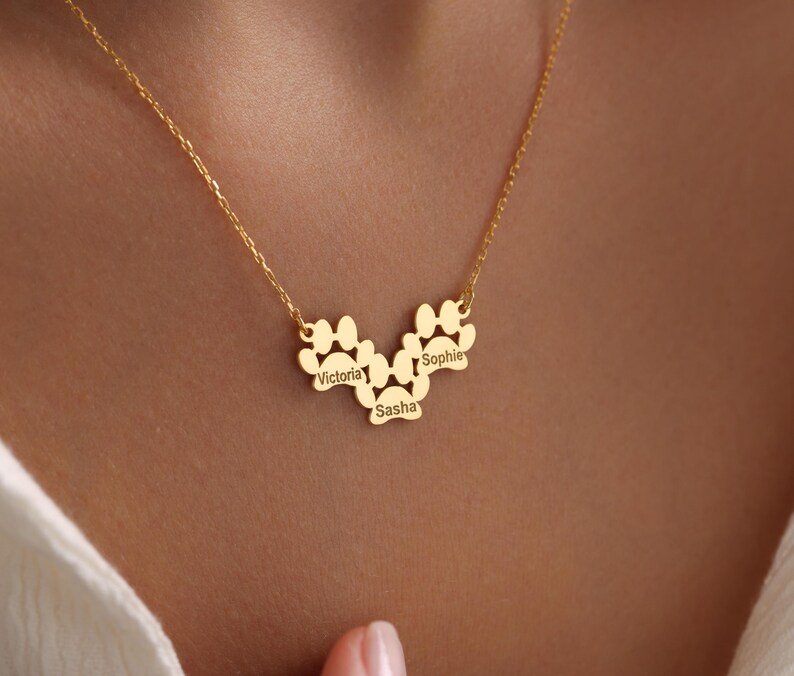 May include: Gold necklace with three paw print charms, each with a name engraved on it: Victoria, Sasha, and Sophie.