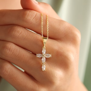 May include: A gold chain necklace with a small, clear crystal cross pendant.
