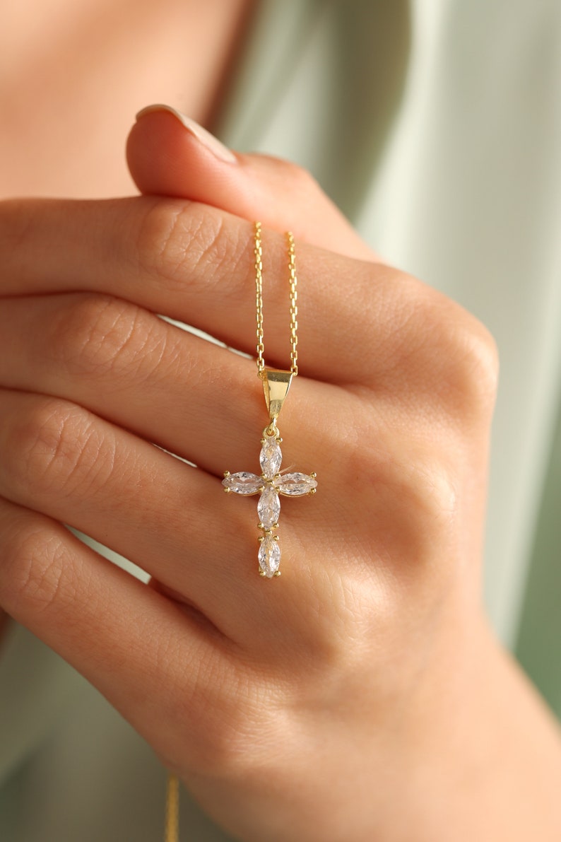 May include: A gold chain necklace with a small, clear crystal cross pendant.