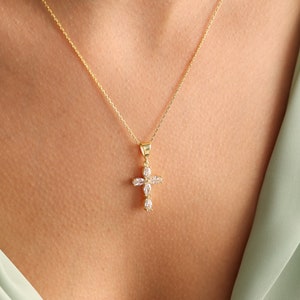 May include: A gold chain necklace with a small, clear crystal cross pendant.