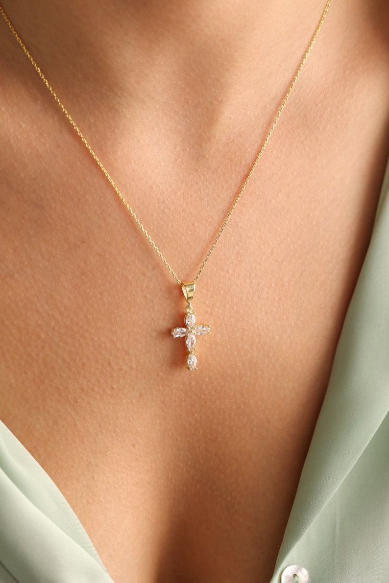 May include: A gold chain necklace with a small, clear crystal cross pendant.