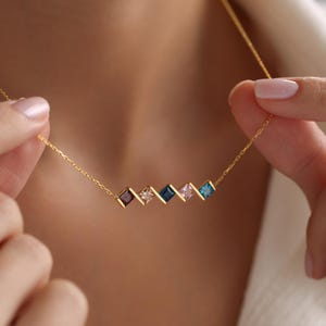 May include: A gold chain necklace with a row of five square-shaped gemstones in shades of blue, pink, and purple.