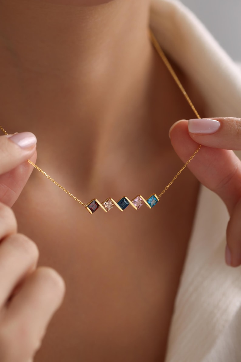 May include: A gold chain necklace with a row of five square-shaped gemstones in shades of blue, pink, and purple.