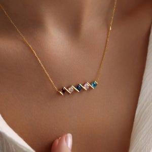 May include: A gold chain necklace with a row of colorful square-shaped gemstones. The gemstones are arranged in a staggered pattern and are set in gold.