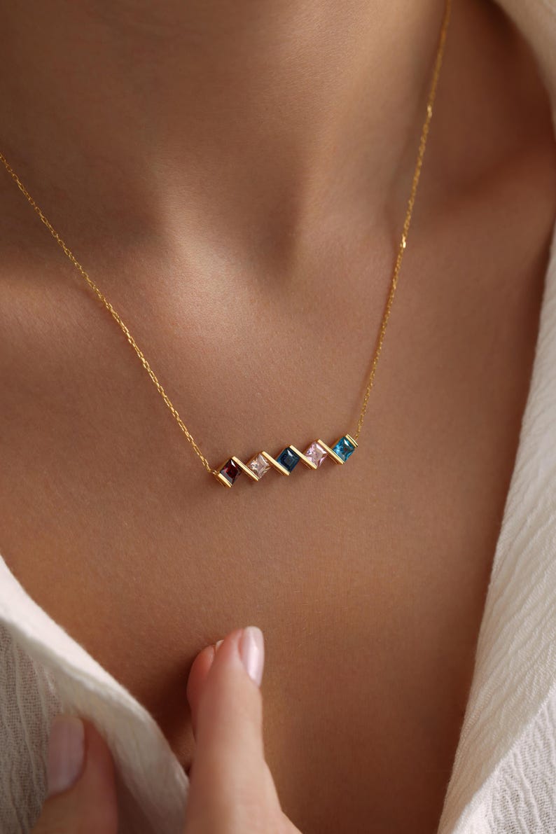May include: A gold chain necklace with a row of colorful square-shaped gemstones. The gemstones are arranged in a staggered pattern and are set in gold.