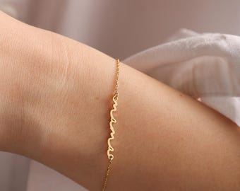May include: A gold chain bracelet with the word "mama" spelled out in a cursive font.