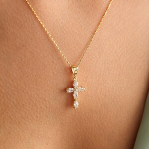 May include: A gold chain necklace with a small, clear crystal cross pendant.