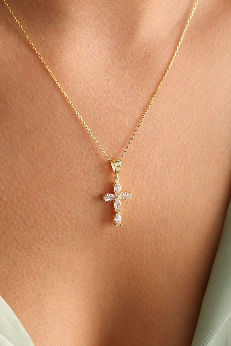 May include: A gold chain necklace with a small, clear crystal cross pendant.