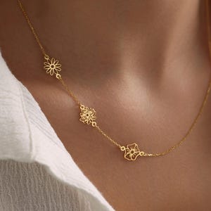 May include: A gold chain necklace with three delicate flower charms. The necklace is made of a thin chain and features a simple design.