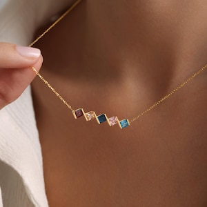May include: A gold chain necklace with a row of five square-shaped gemstones in shades of blue, pink, and red.