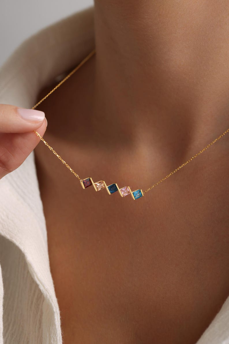 May include: A gold chain necklace with a row of five square-shaped gemstones in shades of blue, pink, and red.