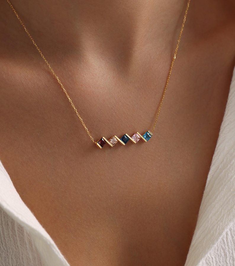 May include: A gold chain necklace with a row of colorful square-shaped gemstones. The stones are arranged in a staggered pattern and are set in gold.