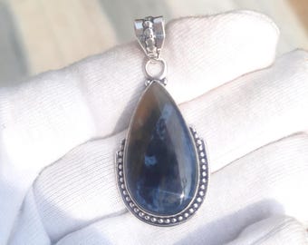 Puede incluir: Un colgante en forma de lágrima con una piedra preciosa azul y marrón engastada en un marco de plata con un borde de cuentas.