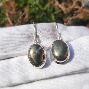 May include: A pair of silver dangle earrings with oval-shaped green gemstone accents.