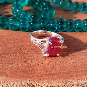 K&ouml;nnte beinhalten: Ein silberner Ring mit einem gro&szlig;en, facettierten, roten Rubin-Edelstein. Der Ring hat ein zartes, filigranes Design mit einem gedrehten Band.