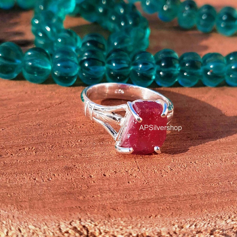 K&ouml;nnte beinhalten: Ein silberner Ring mit einem gro&szlig;en, facettierten, roten Rubin-Edelstein. Der Ring hat ein zartes, filigranes Design mit einem gedrehten Band.