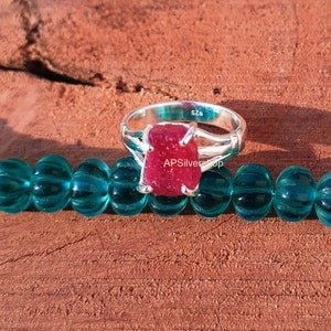 K&ouml;nnte beinhalten: Ein silberner Ring mit einem gro&szlig;en, roten, facettierten Rubin-Edelstein. Der Ring ist mit der Gr&ouml;&szlig;e "SZ6" gekennzeichnet.