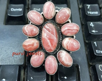 May include: A silver ring with a pink and white gemstone cluster in a flower shape. The ring is on a black keyboard.